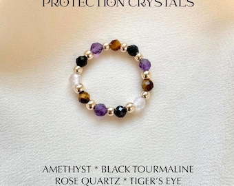 Könnte beinhalten: Ein Perlenring mit facettierten Amethyst-, schwarzem Turmalin-, Rosenquarz- und Tigeraugen-Edelsteinen, durchsetzt mit kleinen goldfarbenen Metallperlen. Der Text PROTECTION CRYSTALS und AMETHYST * BLACK TOURMALINE ROSE QUARTZ * TIGER'S EYE ist sichtbar.
