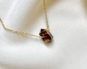 May include: A delicate gold-tone chain necklace featuring a single, faceted, hexagonal-shaped tiger's eye gemstone pendant. The brown and gold striped stone is suspended directly on the thin metal link chain, creating a simple, refined piece.