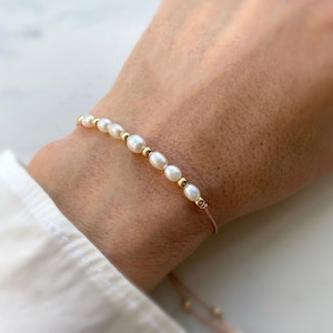 May include: A delicate bracelet with a string of small white pearls and gold beads.