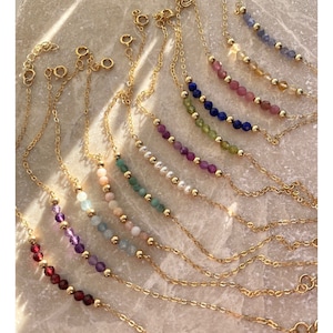 Peut inclure: Une collection de bracelets à chaîne dorée délicats, chacun présentant une rangée centrale de petites perles de pierres précieuses facettées multicolores et de minuscules perles d'espacement dorées. Chaque bracelet possède un fermoir à ressort.