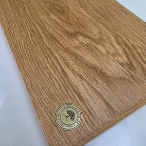 May include: A rectangular wooden cutting board with a natural wood grain finish. A circular brass emblem with the text "Foundry & Forest Est. 2026" is affixed to the board. The board is likely used for food preparation.