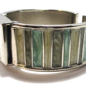 May include: Silver-toned hinged cuff bracelet with a rectangular design. The bracelet features vertical panels in shades of green and beige. The bracelet is a fashion accessory.