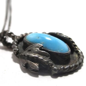 May include: A silver pendant necklace featuring a bright turquoise oval stone. The stone is set in a decorative, oxidized silver setting with a rope-like border and leaf accents. The chain is also silver.