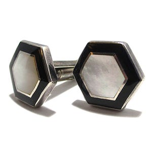 May include: A pair of cufflinks with a hexagonal design. Each cufflink features a black border, a silver-colored frame, and a white, pearlescent center. The cufflinks are displayed on a white background.