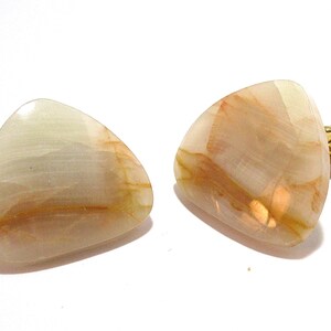 May include: A pair of cufflinks with a triangular shape. The cufflinks are made of a light-colored stone with brown and tan veining. The metal hardware is gold-colored.