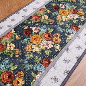 Può includere: Runner da tavolo floreale con sfondo verde scuro, con rose arancioni, gialle e bianche, e fiori blu. Bordo grigio con motivo floreale e rilegatura grigia. Lunghezza di circa 150 cm.