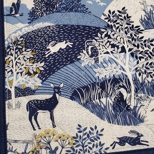 May include: A quilted fabric with a nature scene in shades of blue and white. The design features a deer, rabbits, an owl, trees, and birds. The fabric is bordered with a dark blue trim.