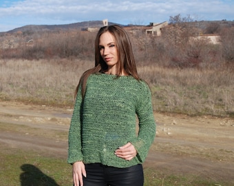 May include: A green knitted sweater with a loose fit and a slightly dropped shoulder. The sweater is made of a soft, textured yarn.