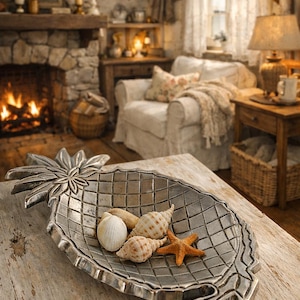 May include: A silver pineapple-shaped serving dish filled with seashells and a starfish sits on a rustic wooden table. The dish has a grid pattern and is surrounded by a cozy living room setting with a fireplace.