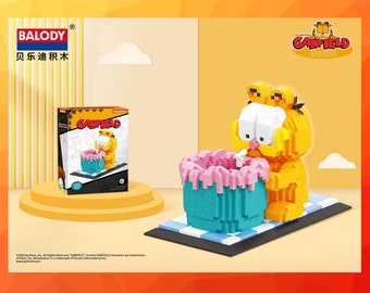 May include: A yellow Garfield block figure with a pink and blue cake, part of a building block set. The box shows the Garfield character and the cake. The set is from the BALODY brand.