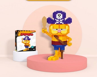 May include: A Garfield pirate-themed building block figure, featuring a yellow and orange design with a blue hat and shorts. The figure holds a wooden sword. A box with the Garfield logo is also present.