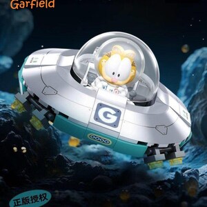 May include: A Garfield figure in a space-themed vehicle. The vehicle is silver and teal with the letter "G" on the side. The image includes the text "Travel in space with Garfield" and the Garfield logo.