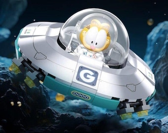 May include: A Garfield figure in a space-themed vehicle. The vehicle is silver and teal with the letter "G" on the side. The image includes the text "Travel in space with Garfield" and the Garfield logo.