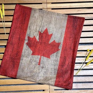 May include: A red and white Canadian flag pillow with a distressed look. The flag features a red maple leaf on a white background.