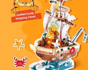 May include: A toy boat featuring Garfield and friends. The brown and white boat has a mast, sails, and a crane. The text "Sea Voyage" and "Voyager" are visible. The set includes a red crab and a yellow starfish.