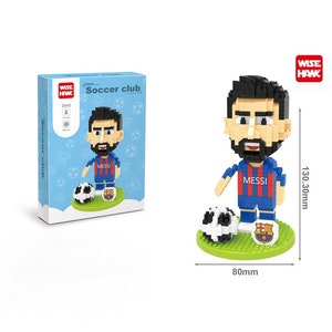 May include: A block figure of a soccer player in a blue and red jersey with the name "MESSI". The figure is on a green base with a soccer ball and a team logo. The figure is 130.30mm tall and the base is 80mm wide. The box says "Soccer club".