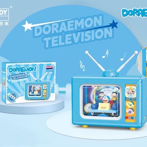 May include: A light blue Doraemon television toy with white aerials and a screen displaying cartoon characters. The box next to it also shows the toy. The words "Doraemon Television" are written on the background.