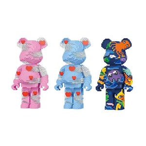 May include: Three colorful bear-shaped figurines. The first is pink with red hearts, the second is light blue with red hearts, and the third is dark blue with a colorful design. All have silver accents.