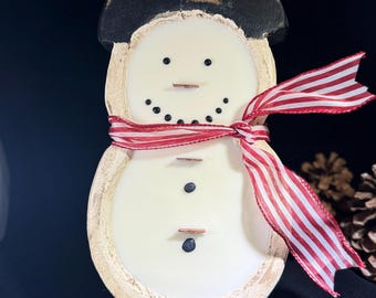 May include: A wooden snowman figurine with a black top hat and a red and white striped scarf. The snowman has a white body with black dot eyes and a twig mouth. A festive winter decoration.