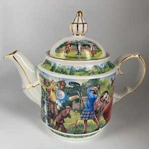 May include: A white porcelain teapot with a gold trim and a lid featuring a colorful illustration of golfers and the text "Golfing Heroes".