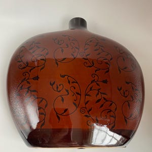 May include: A brown ceramic vase with a rounded shape and a black floral design. The vase has a glossy finish.