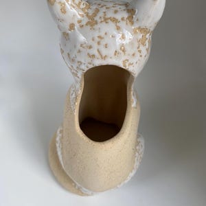 May include: A ceramic fox-shaped planter in a sitting position. The planter is mainly beige with white accents and a speckled, textured finish. The fox's ears and head are white with brown speckles, and the interior is hollow.