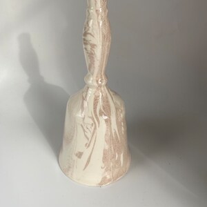 May include: A ceramic bell with a white and brown marbled design. The bell has a long handle and a flared base. The color scheme is neutral, with the brown marbling adding visual interest. The bell is likely handmade and suitable for home decor.