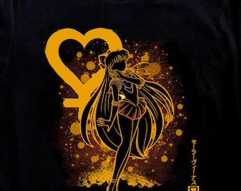 May include: Black t-shirt featuring a gold silhouette of a female anime character with long hair, a heart-shaped symbol, and Japanese text. The design includes a gold and brown speckled background. Black and white sneakers are in the foreground.