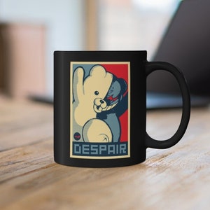 Può includere: Tazza da caffè nera con un'immagine di un orso di cartone animato bianco e nero. L'immagine è in una cornice rosso, bianco e blu con la parola "DESPAIR" stampata sotto.