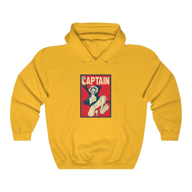 K&ouml;nnte beinhalten: Gelber Hoodie mit einer roten und blauen Grafik eines Comic-Charakters mit dem Wort "CAPTAIN" &uuml;ber dem Charakter.