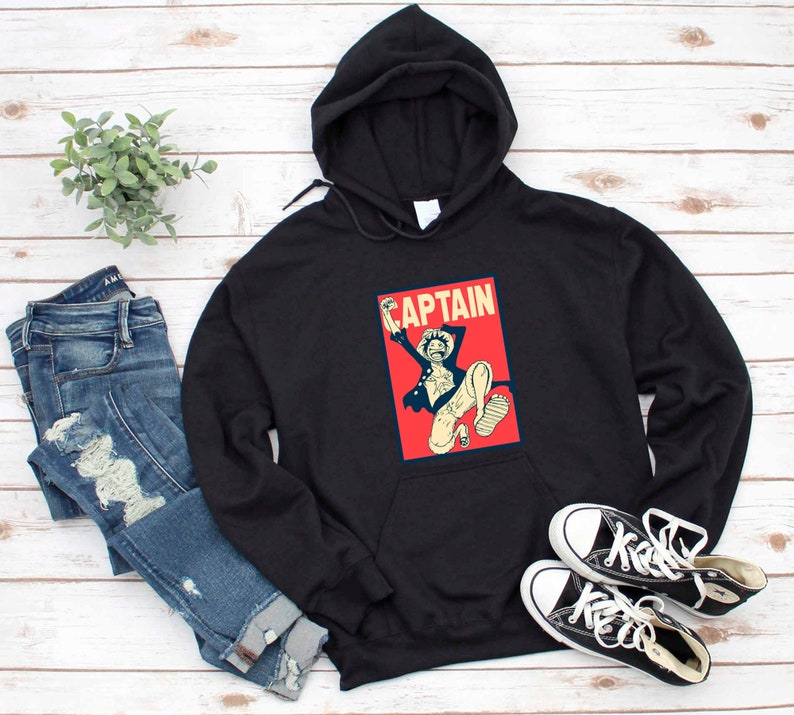 K&ouml;nnte beinhalten: Schwarzer Kapuzenpullover mit einem roten und wei&szlig;en Grafikdruck eines Comic-Charakters mit dem Text "CAPTAIN" auf der Vorderseite.