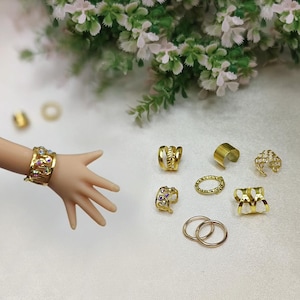 May include: A set of eight gold-toned jewellery pieces, including rings, bracelets, and ear cuffs. Some pieces feature intricate designs and sparkling rhinestones.