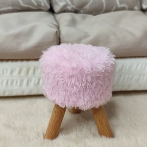 K&ouml;nnte beinhalten: Ein kleiner, flauschiger Hocker in Rosa mit Holzbeinen. Der Hocker steht auf einem wei&szlig;en, flauschigen Teppich. Der Buchstabe "B" ist in Rosa auf den Teppich gedruckt.