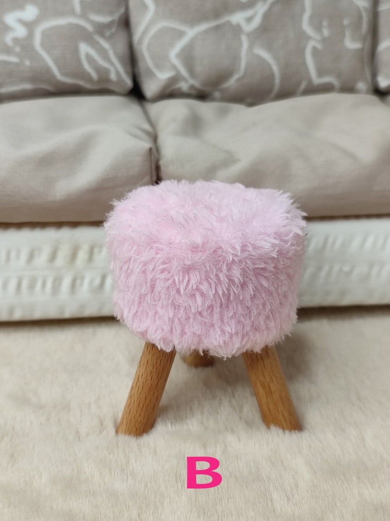 K&ouml;nnte beinhalten: Ein kleiner, flauschiger Hocker in Rosa mit Holzbeinen. Der Hocker steht auf einem wei&szlig;en, flauschigen Teppich. Der Buchstabe "B" ist in Rosa auf den Teppich gedruckt.