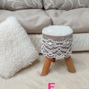 K&ouml;nnte beinhalten: Ein wei&szlig;er Hocker mit einer Spitzenbezug und Holzbeinen. Der Hocker steht auf einem wei&szlig;en, flauschigen Teppich. Der Buchstabe "F" ist in Pink auf den Teppich geschrieben.