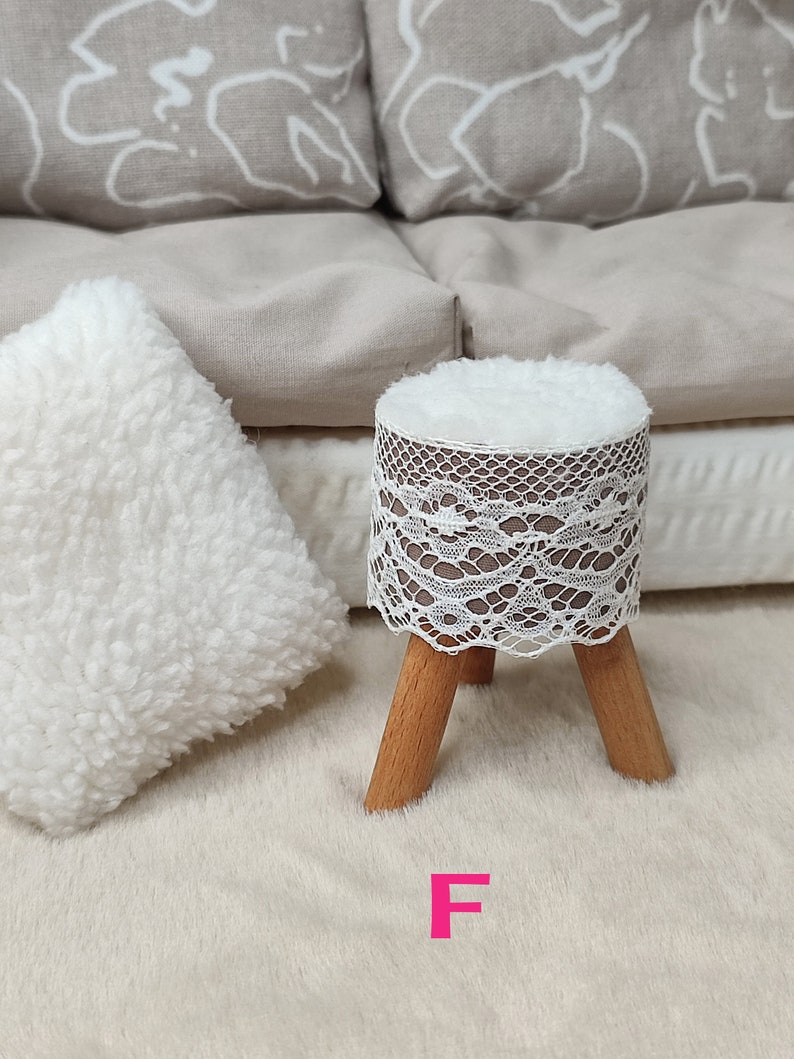 K&ouml;nnte beinhalten: Ein wei&szlig;er Hocker mit einer Spitzenbezug und Holzbeinen. Der Hocker steht auf einem wei&szlig;en, flauschigen Teppich. Der Buchstabe "F" ist in Pink auf den Teppich geschrieben.
