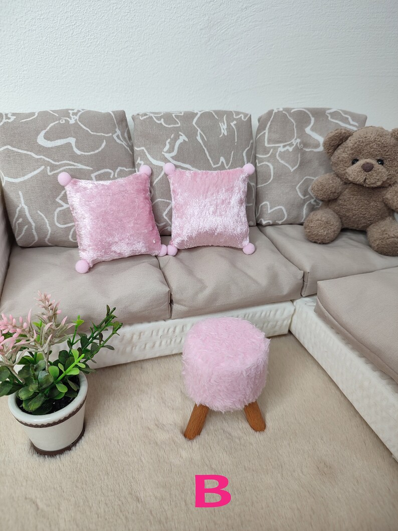 K&ouml;nnte beinhalten: Ein wei&szlig;es Sofa mit drei beigen Kissen und zwei rosa Samtkissen. Ein brauner Teddyb&auml;r sitzt auf dem Sofa. Ein rosa, flauschiger Hocker mit Holzbeinen steht vor dem Sofa. Eine kleine Topfpflanze steht auf dem Boden vor dem Sofa.
