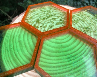 May include: Set of four green and orange hexagonal coasters with a glittery finish. The coasters are arranged in a honeycomb pattern on a wooden surface.