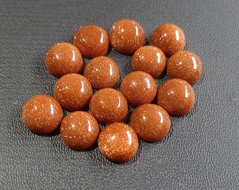 May include: A collection of 15 smooth, round, orange-brown gemstone cabochons. The cabochons have a sparkly, speckled texture.
