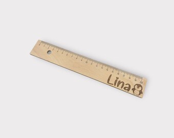 May include: A wooden ruler with a penguin design and the name "Lina" engraved on it. The ruler is 50.8 cm long and has markings for each centimetre.