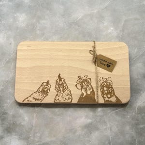 May include: A rectangular wooden chopping board featuring four engraved chicken designs. The chickens are adorned with accessories such as glasses and bows. A small tag tied with twine reads "made with love."