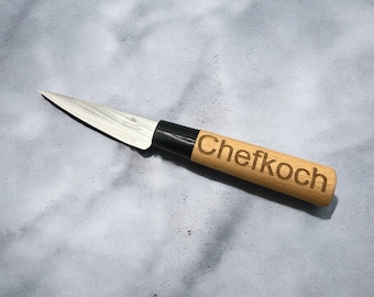 May include: A small, silver paring knife with a wooden handle. The handle is engraved with the word "Chefkoch".