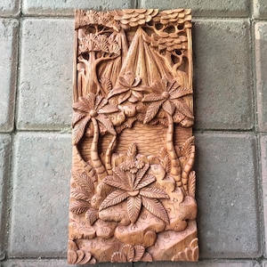 May include: A rectangular, intricately carved wooden wall art piece depicting a tropical landscape. The relief carving features palm trees, mountains, and other foliage. The artwork is in shades of brown and tan, showcasing the natural wood grain.