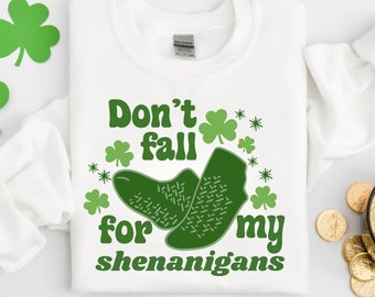 Puede incluir: Camiseta blanca con un trébol verde y texto que dice "No te dejes engañar por mis travesuras".