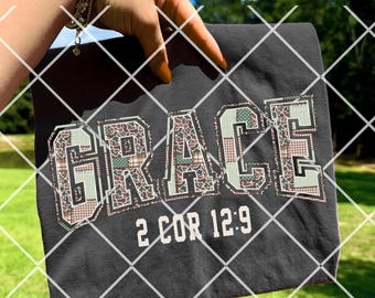 Könnte beinhalten: Dunkelgraues T-Shirt mit dem Wort "GRACE" in einem Patchwork-Design mit grünen, braunen und beigen Mustern. Der Text "2 COR 12:9" steht unter "GRACE" in Weiß. Das T-Shirt wird vor einem Hintergrund aus grünem Gras und blauem Himmel gehalten.