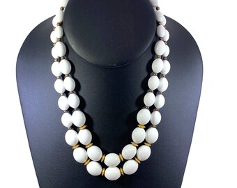 May include: A double strand white bead necklace with gold accents. The beads are oval shaped and the necklace is displayed on a black mannequin.