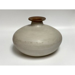 May include: A white ceramic vase with a brown rim. The vase has a rounded, bulbous shape.