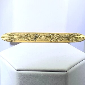 Könnte beinhalten: Ein goldfarbener Krawattenclip mit einem Weizenähren-Design. Die Weizenähren sind in der Mitte mit einer Schleife zusammengebunden.