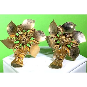 Puede incluir: Un par de pendientes de clip de tono dorado con dise&ntilde;o floral. Los pendientes est&aacute;n hechos de metal y tienen un patr&oacute;n floral con una piedra central.