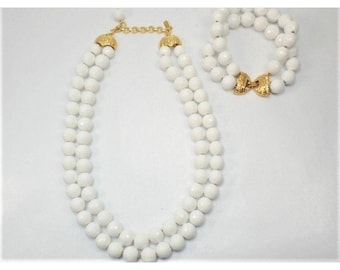 May include: A white two-strand necklace and bracelet set made of faceted beads with gold-toned clasps.